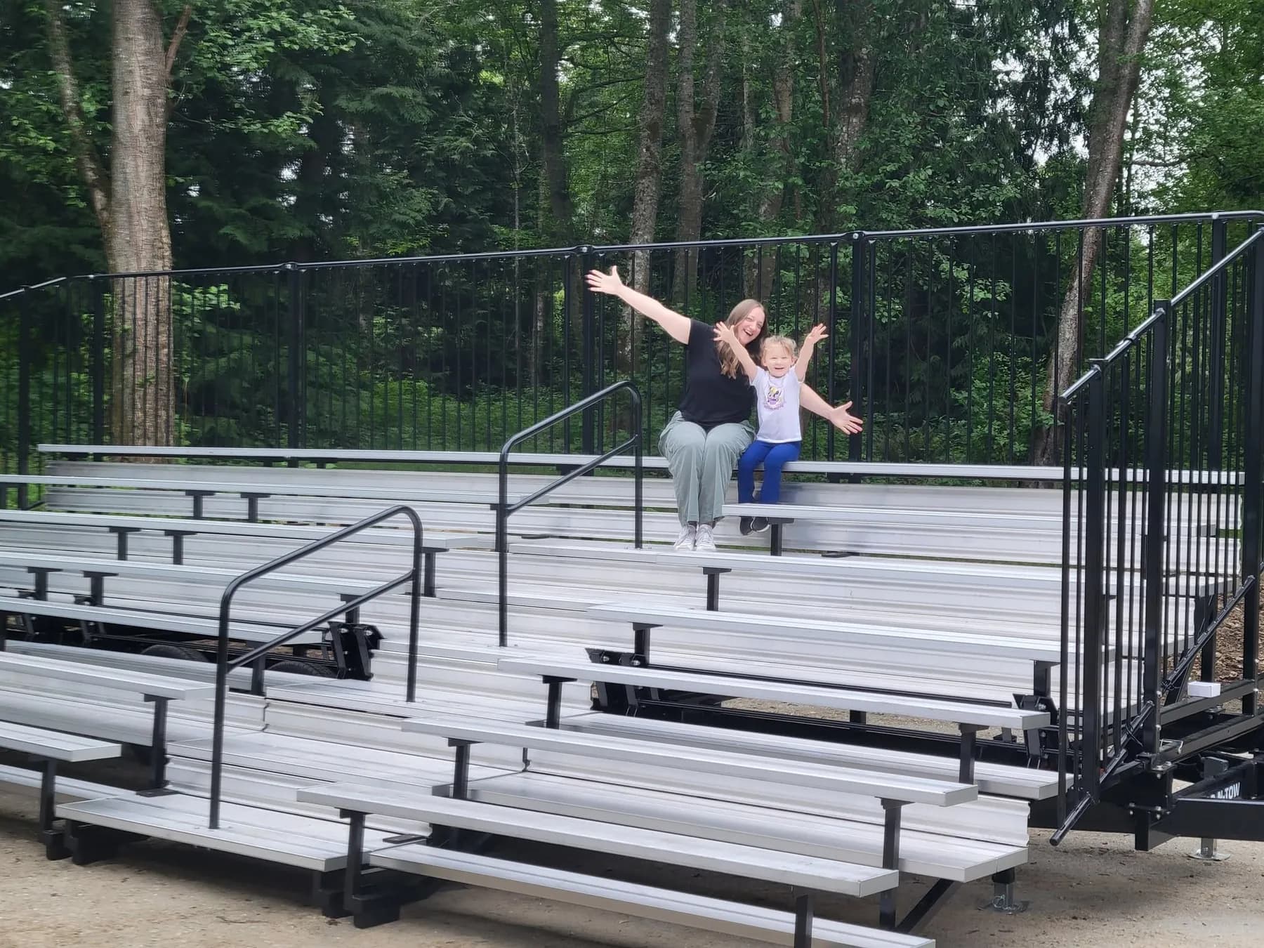 A mom and daughter smiling with arms raised on Bleachers NW portable bleachers at an outdoor venue